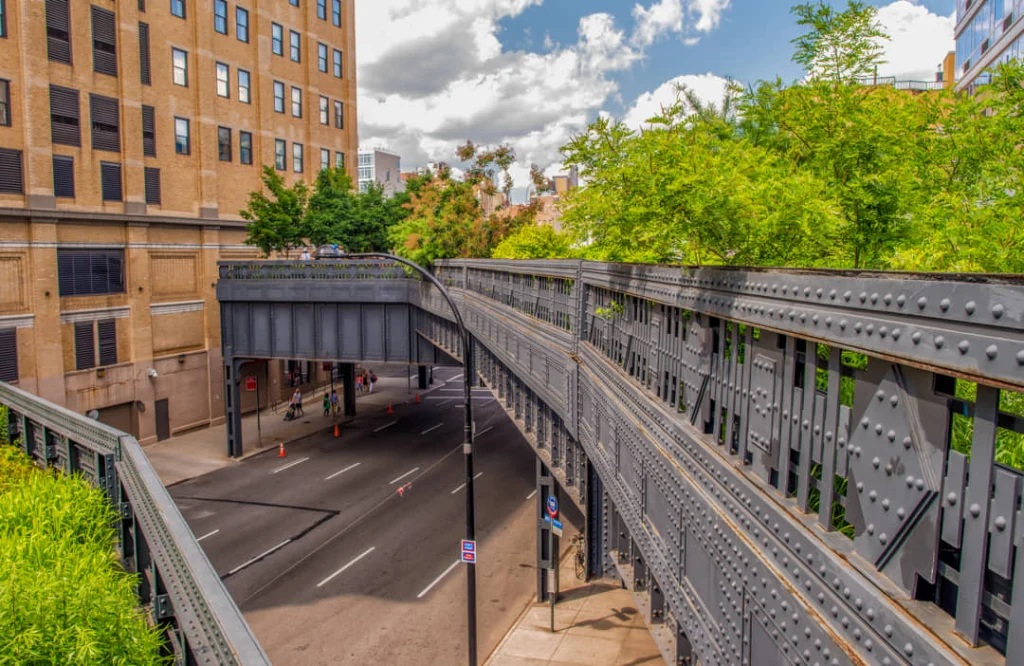 Uitzicht over het verhoogde stalen spoorviaduct van de High Line dat over een brede straat in New York loopt, met groen aan weerszijden