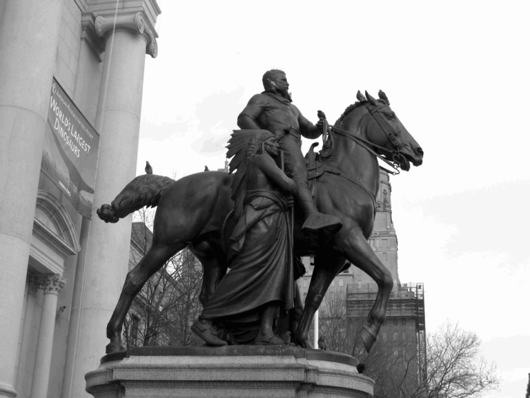 Zwart wit beeld van het ruiterstandbeeld van Theodore Roosevelt bij de ingang van het American Museum of Natural History in New York, met zuilen en een aankondiging voor een dinosaurustentoonstelling