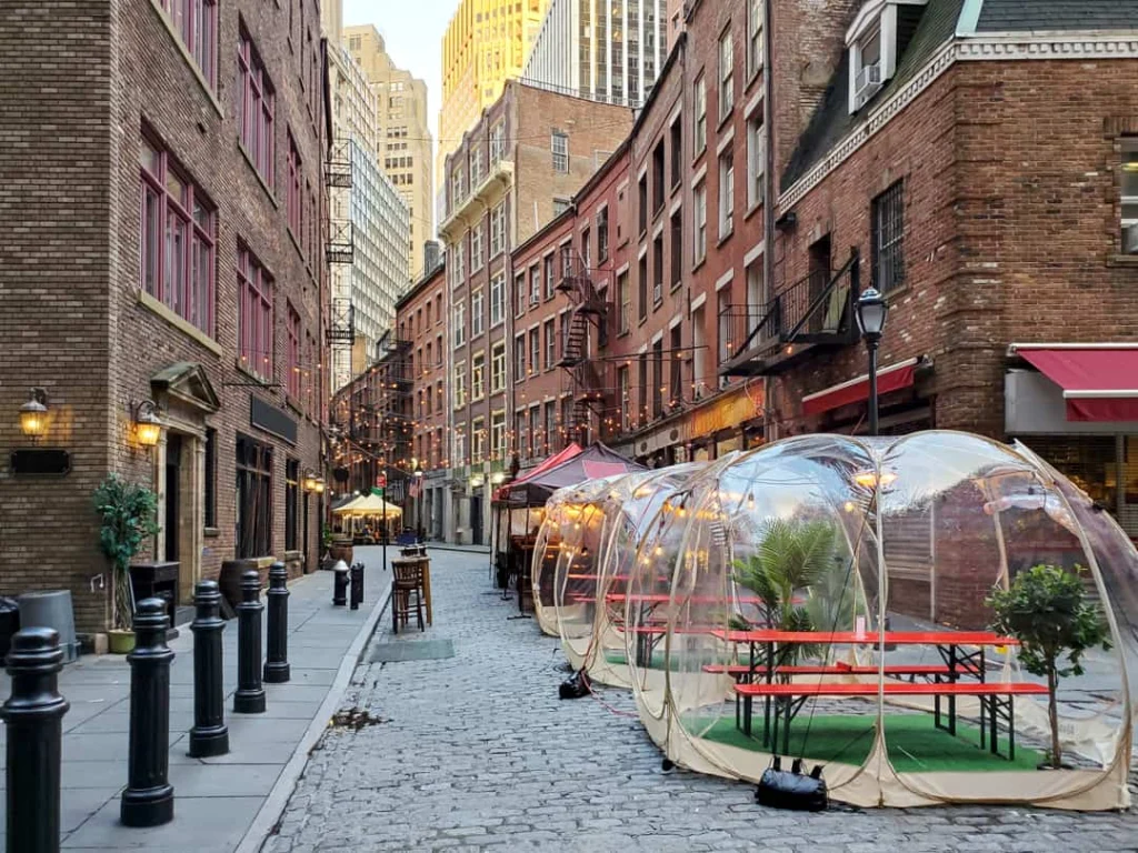 Kasseienstraat Stone Street in New York met een rij doorzichtige eetbubbels met tafels langs de bakstenen gevels bij avondlicht