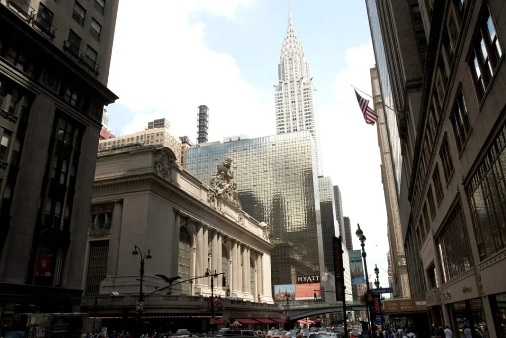 Gevel van Grand Central Terminal gezien vanaf een drukke straat met de Chrysler Building, verkeer en een Hyatt hotelbord op de voorgrond