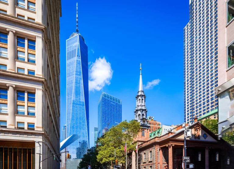 Smalle straat in Lower Manhattan met de glazen spits van One World Trade Center en een kerktoren op de achtergrond