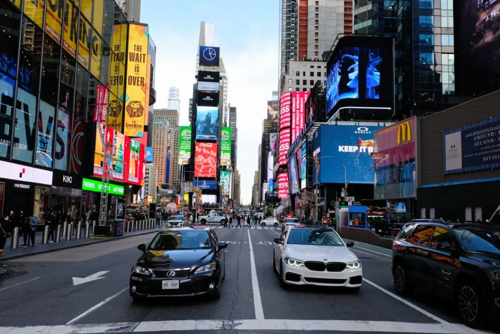 Drukke kruising in Times Square New York overdag met auto's, gele taxi's en grote verlichte reclameborden aan weerszijden van de straat