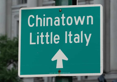 Groen straatbord met witte tekst Chinatown Little Italy en een pijl omhoog, bevestigd aan een lantaarnpaal in New York