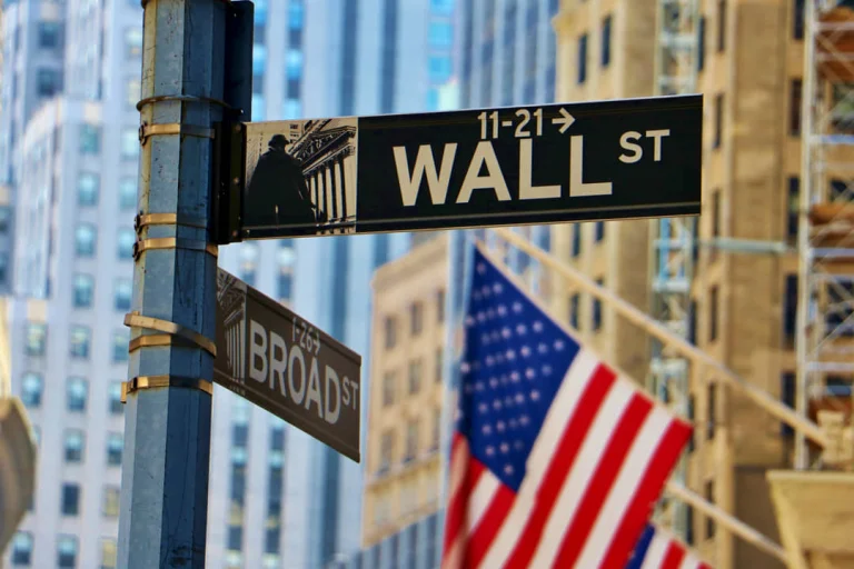 Straatborden van Wall Street en Broad Street bij de gevel van de New York Stock Exchange met een Amerikaanse vlag