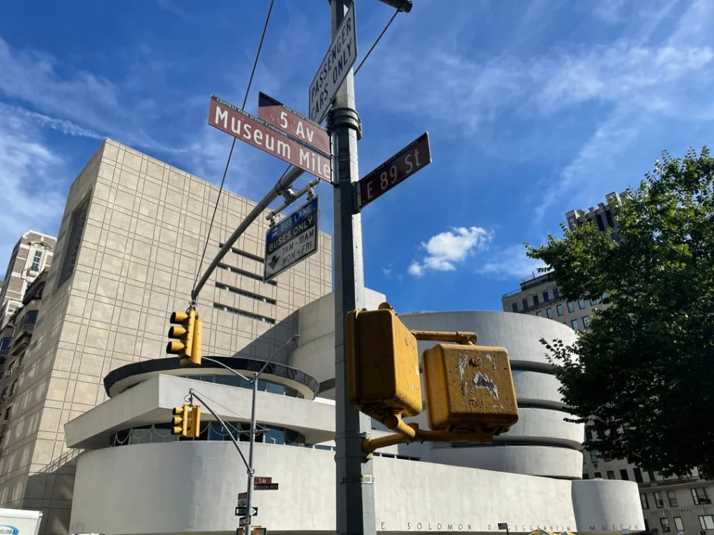 Straatbordjes met de tekst 5 Av, Museum Mile en E 89 St met de ronde gevel van het Guggenheim Museum op de achtergrond