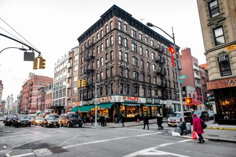 Drukke straathoek in Little Italy in New York met een bakstenen hoekgebouw, winkel Di Palo's en verkeer op straat