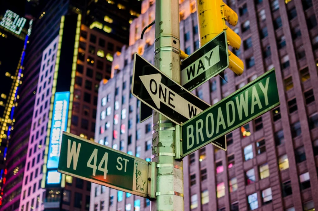 Straatnaambordjes voor Broadway en West 44th Street bij een verkeerslicht in Times Square New York, met verlichte wolkenkrabbers op de achtergrond in de avond
