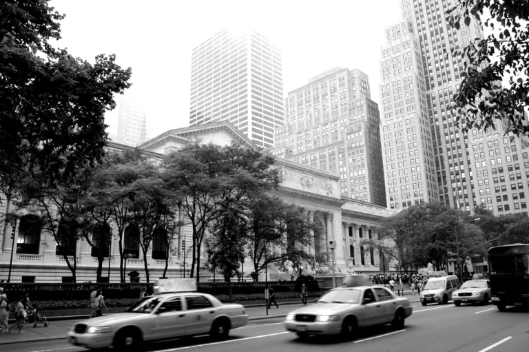 Zwart wit straatbeeld met gele taxi's op Fifth Avenue voor de New York Public Library, omringd door wolkenkrabbers