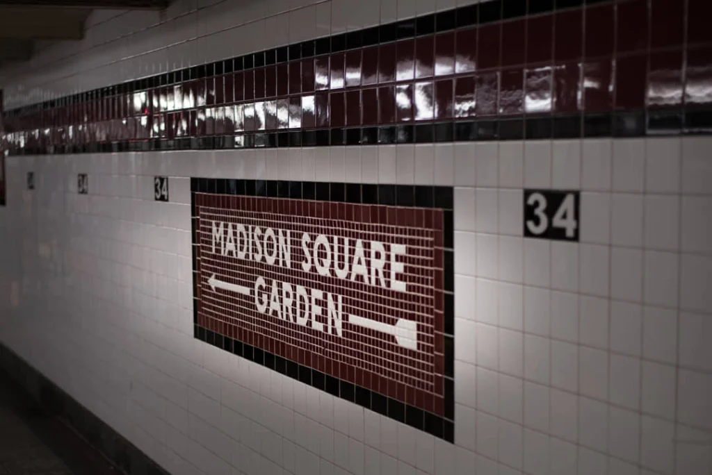 Wit betegelde metrogang in New York met een bruin tegelbord en pijl richting Madison Square Garden