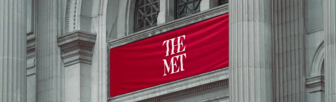 Close-up van een rode banier met de tekst The Met tussen de stenen zuilen van de gevel van het Metropolitan Museum of Art in New York