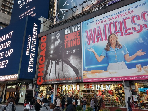 Felgekleurde billboards voor de musicals Chicago en Waitress boven winkels en voorbijgangers op Times Square in New York