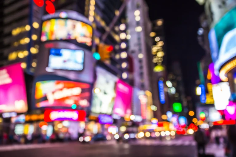 Onscherpe opname van felgekleurde neonlichten en reclameborden in Times Square New York bij avond, met wazige lichtjes van verkeer op straat