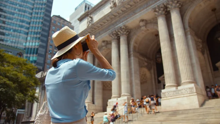 Vrouw met strohoed maakt een foto van de imposante zuilengevel van het Metropolitan Museum of Art in New York, met bezoekers op de trap