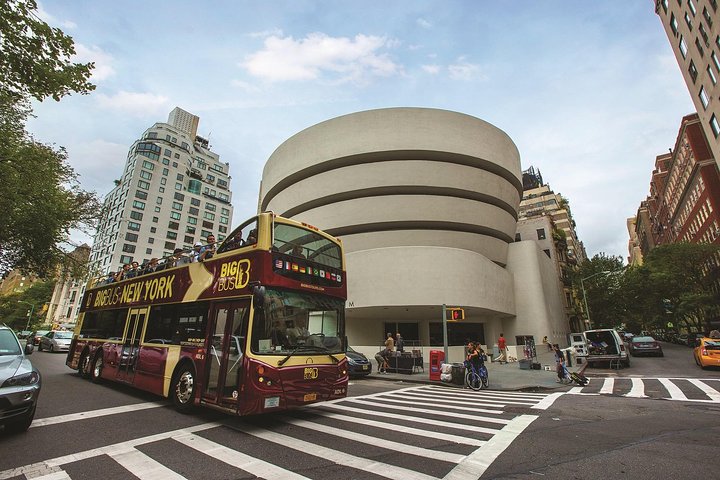Een rode dubbeldekker toeristenbus rijdt langs het ronde gebouw van het Guggenheim Museum in New York