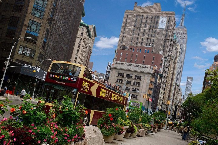Een rode dubbeldekker toeristenbus rijdt door een drukke straat in Manhattan met het Empire State Building op de achtergrond