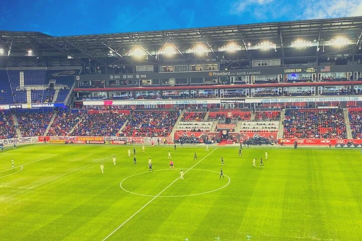 Volle tribune van de Red Bull Arena met spelers die op het veld aan het warmlopen zijn bij avondlicht