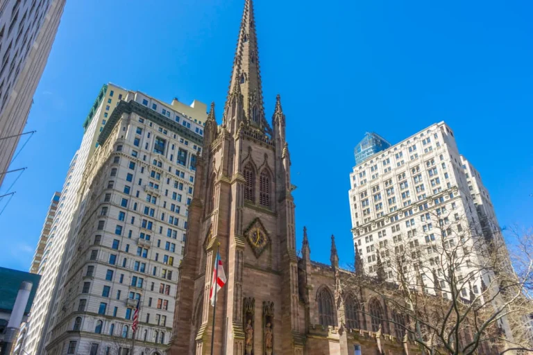 Laag standpunt op de gotische spits van Trinity Church, omringd door wolkenkrabbers van Lower Manhattan onder een heldere blauwe hemel