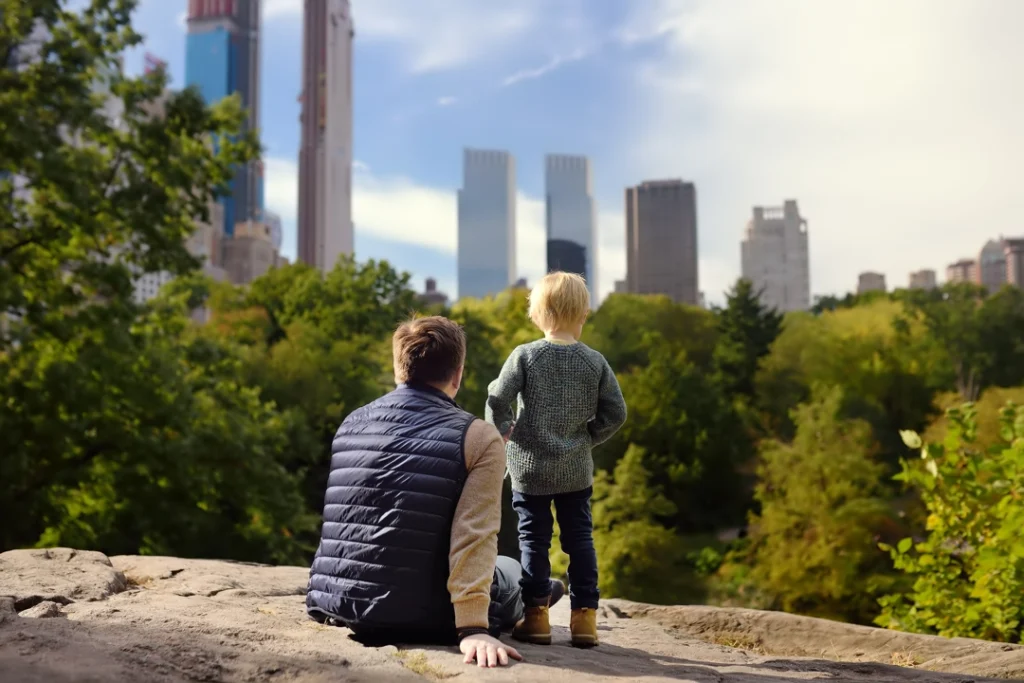Vader en zoon zitten op een rots in Central Park en kijken uit over de bomen naar de wolkenkrabbers