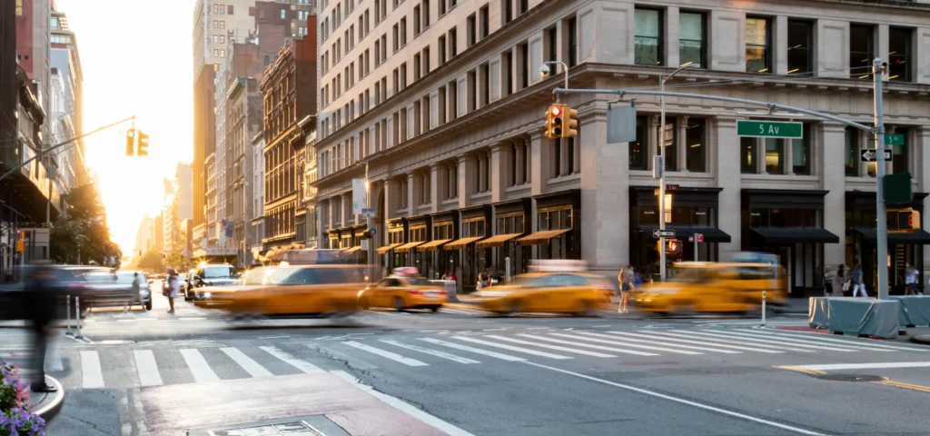Wazig fotograferende gele taxi's steken een kruispunt over bij Fifth Avenue in New York met laag avondlicht tussen de gebouwen