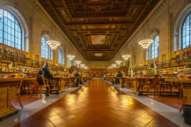 Lange leeszaal met een rijk versierd plafond, kroonluchters en houten leestafels in de New York Public Library
