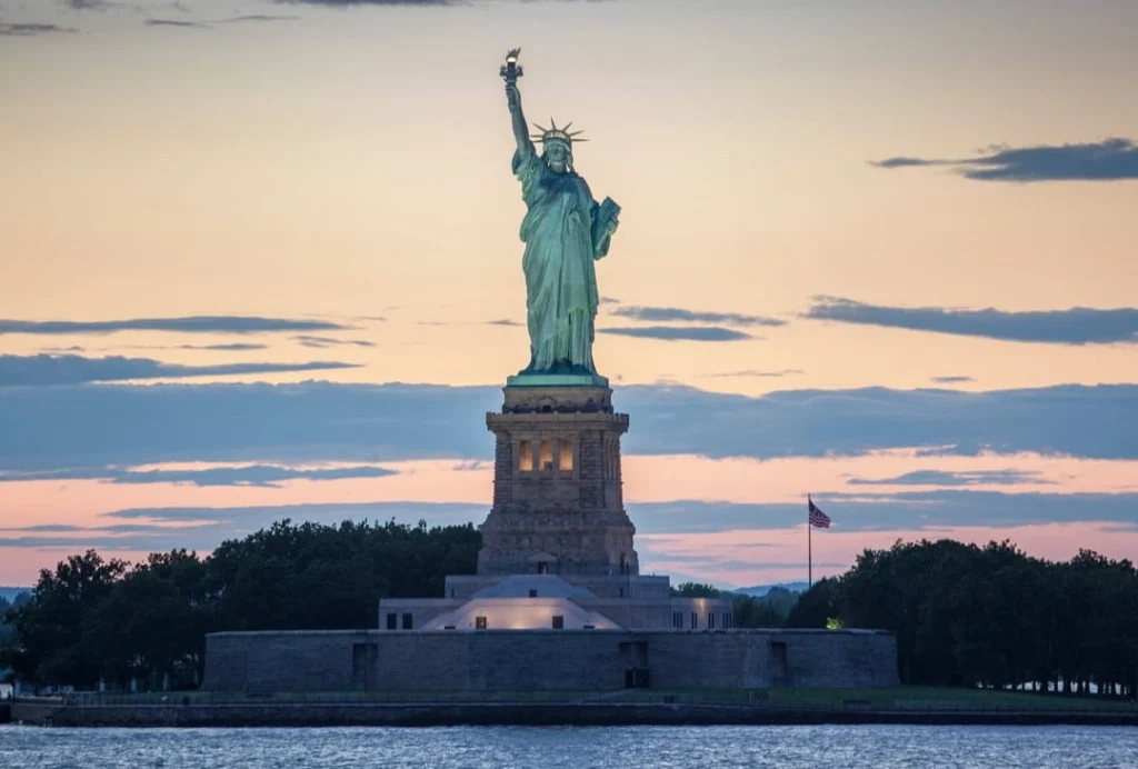 Het groene Vrijheidsbeeld op zijn voetstuk steekt af tegen een roze en blauwe avondlucht in de haven van New York