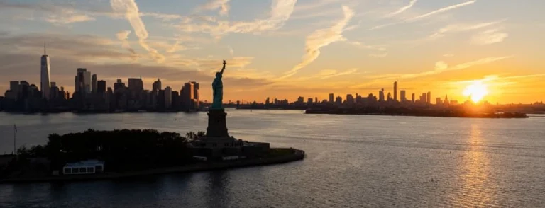 Panoramisch uitzicht op het Vrijheidsbeeld in de haven van New York bij zonsondergang met de skyline van Manhattan en gouden lucht op de achtergrond