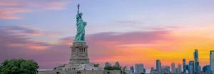 Het Vrijheidsbeeld op Liberty Island bij zonsondergang met een felgekleurde lucht en de skyline van New York op de achtergrond