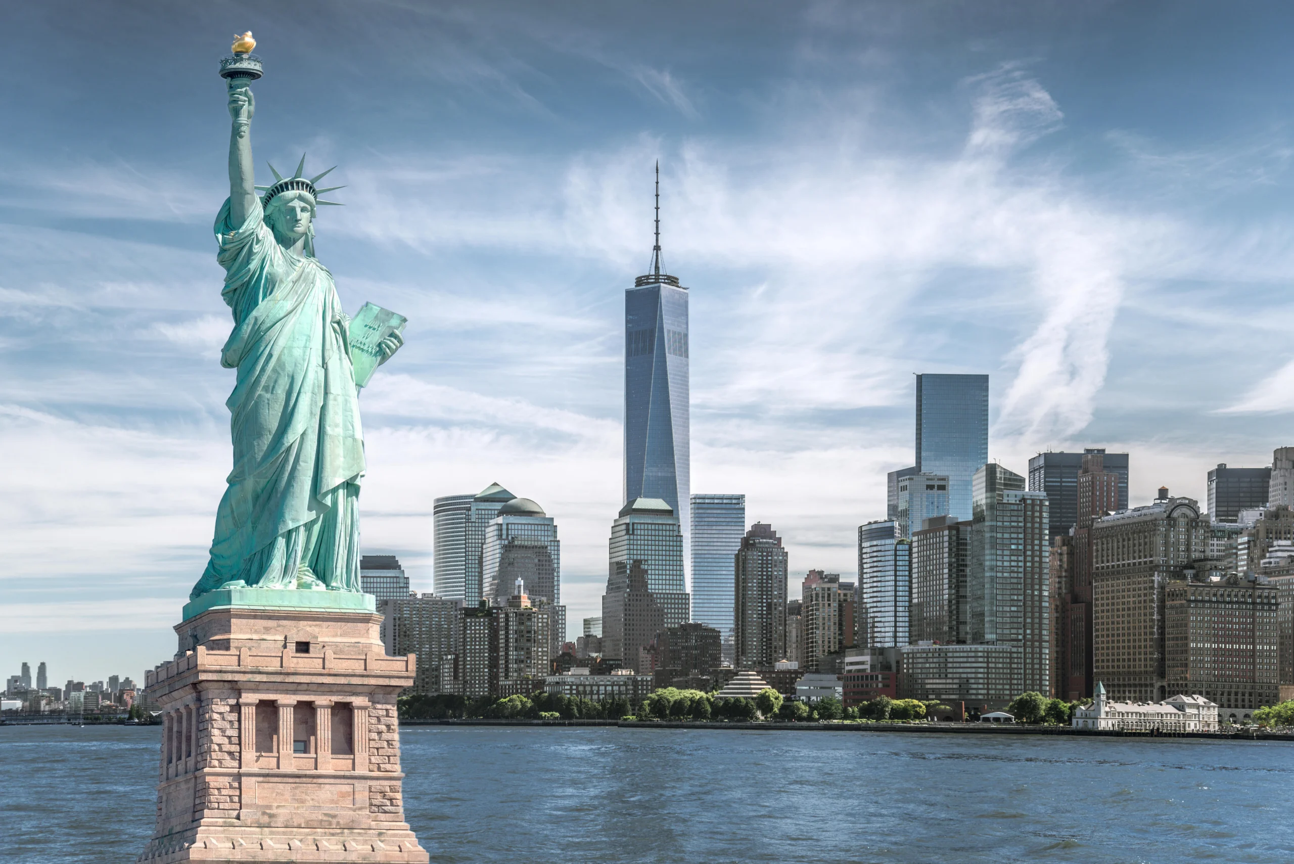 Het Vrijheidsbeeld op zijn sokkel voor het water met de skyline van Manhattan en de One World Trade Center toren in New York