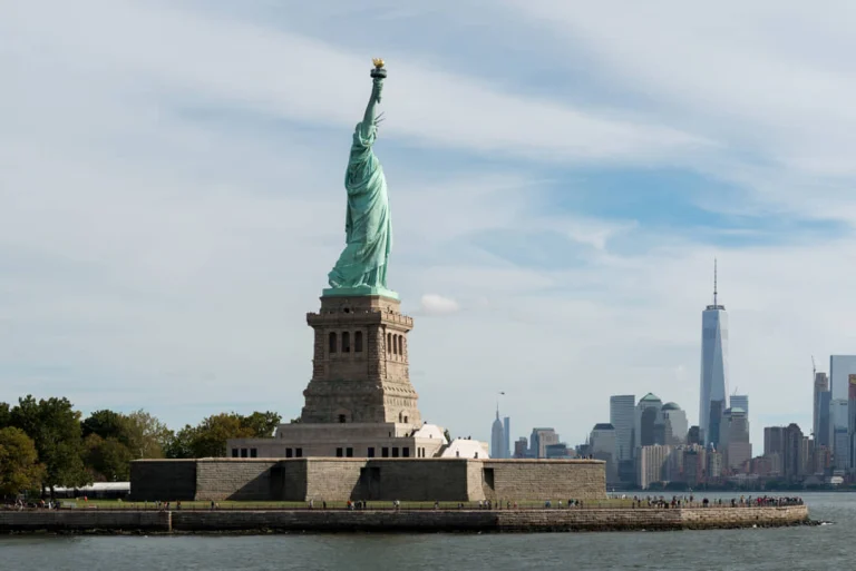 Het groene Vrijheidsbeeld op zijn stenen voetstuk in New York met de skyline van Manhattan en het One World Trade Center in de verte