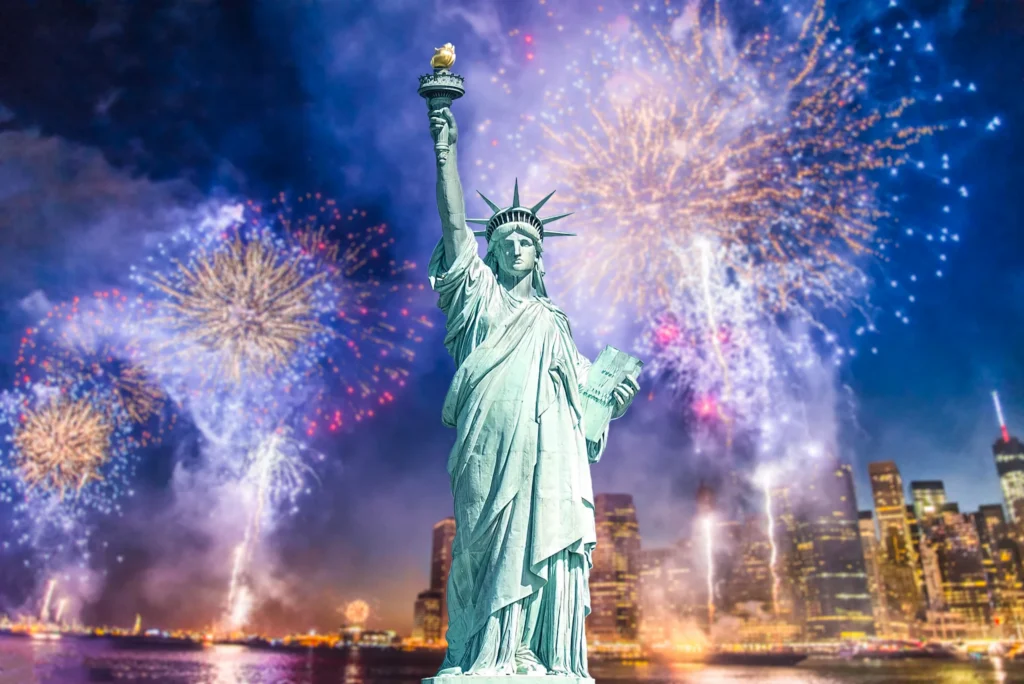 Het Vrijheidsbeeld op de voorgrond met kleurrijk vuurwerk boven de verlichte skyline van New York in de avond