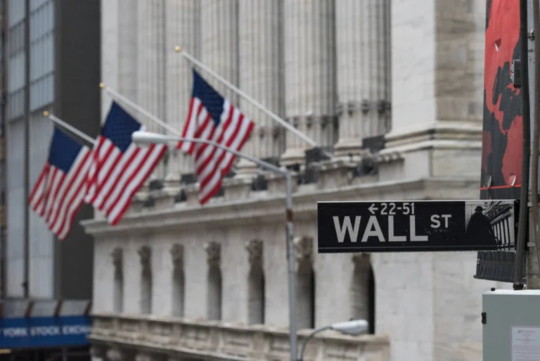 Straatbord met de tekst Wall Street voor de zuilengalerij van de effectenbeurs, versierd met meerdere wapperende Amerikaanse vlaggen