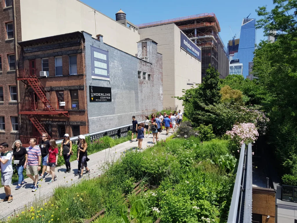 Toeristen lopen over het beplante wandelpad van de High Line in New York met bakstenen gebouwen en een wolkenkrabber in aanbouw op de achtergrond