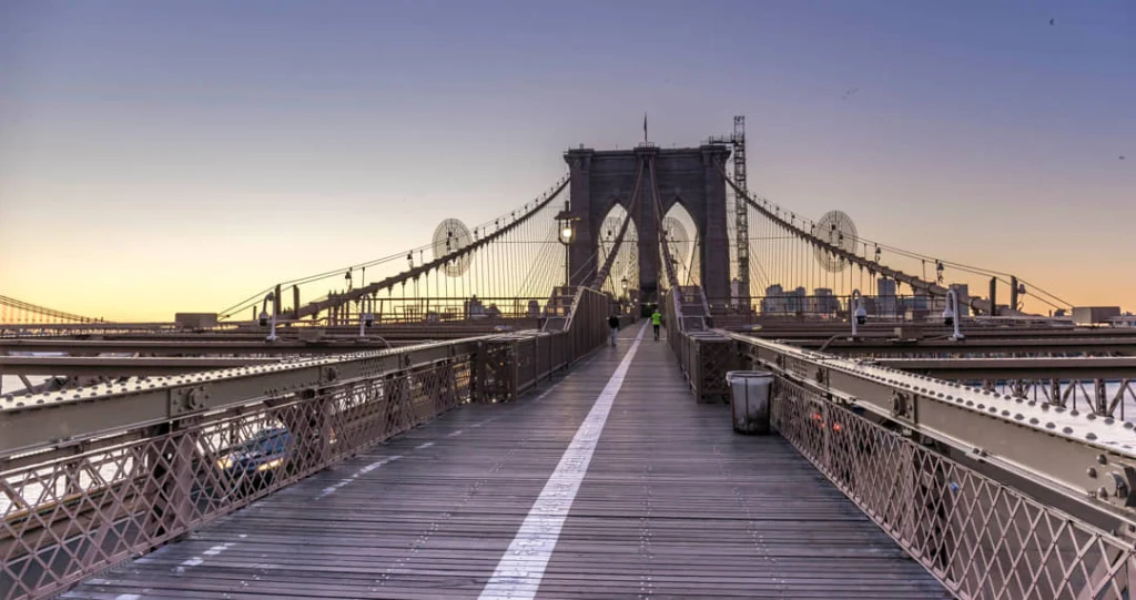 Leeg houten wandelpad over de Brooklyn Bridge met de kenmerkende stenen pilaren en kabels bij zonsopkomst