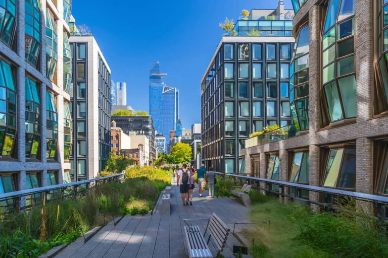 Groen wandelpad van de High Line met bankjes en beplanting tussen glazen kantoorgebouwen met wandelaars op de achtergrond