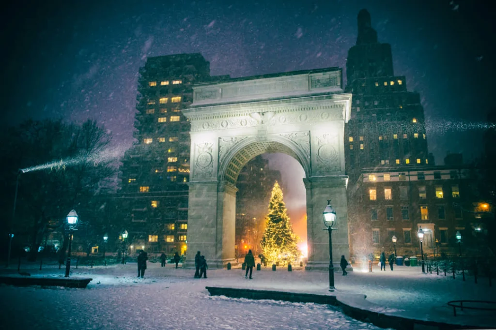 De verlichte Washington Square Arch in New York tijdens een sneeuwbui in de avond met een kerstboom onder de boog