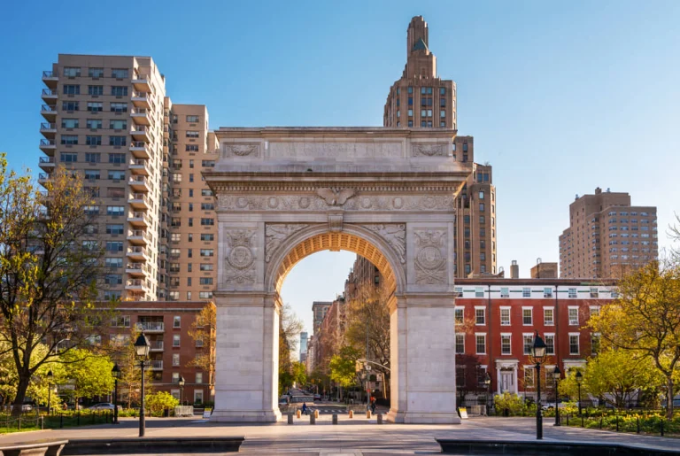 Frontaal zicht op de witte Washington Square boog in New York met bomen en gebouwen aan weerszijden