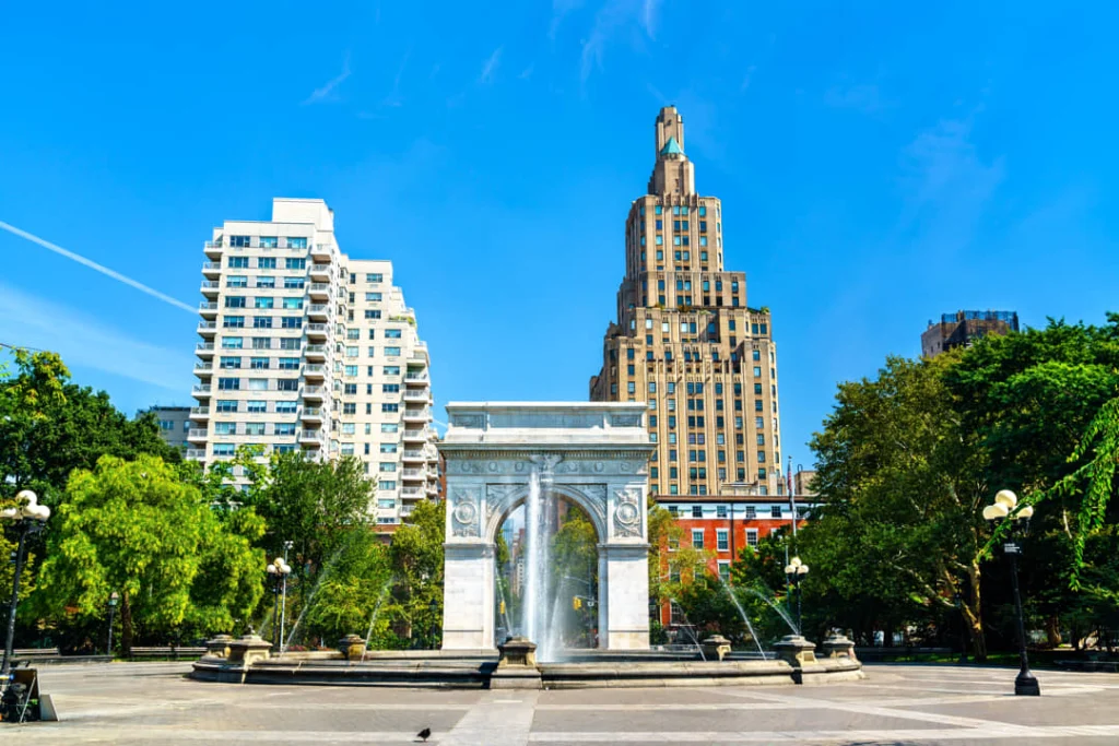 Witte marmeren boog van Washington Square Park in New York met spattend fonteinwater en een hoge woontoren op de achtergrond
