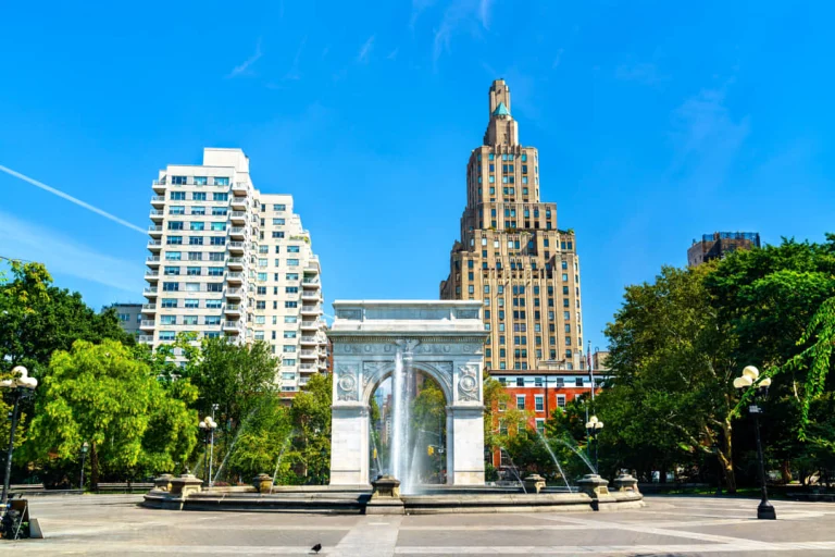 Witte marmeren boog van Washington Square Park in New York met spattend fonteinwater en een hoge woontoren op de achtergrond