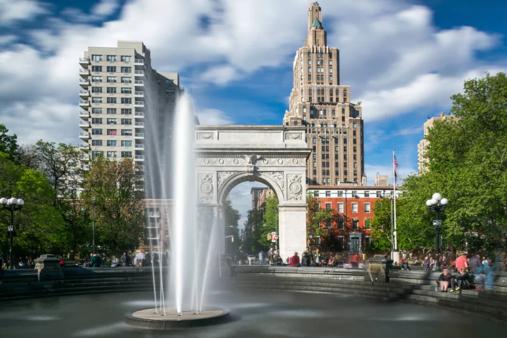 Spuitende fontein voor de witte marmeren boog van Washington Square Park in New York onder een strakblauwe lucht