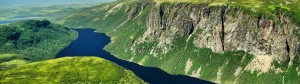 Luchtfoto van een lang smal meer dat kronkelt tussen groene heuvels en steile rotswanden in Newfoundland en Labrador