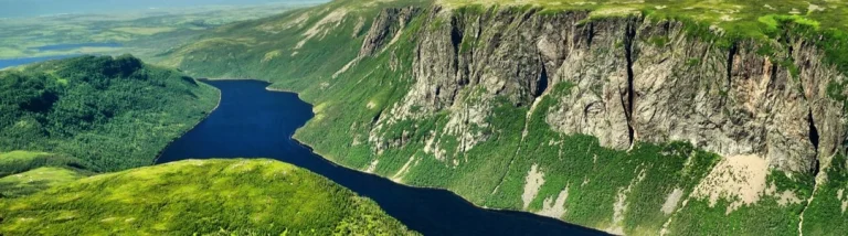 Luchtfoto van een lang smal meer dat kronkelt tussen groene heuvels en steile rotswanden in Newfoundland en Labrador