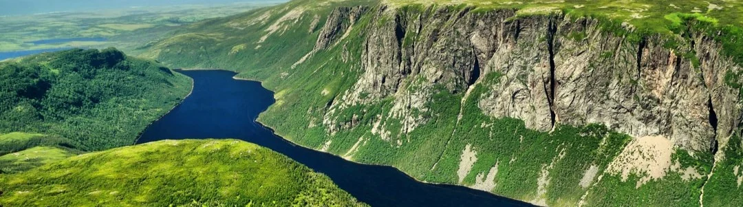 Luchtfoto van een lang smal meer dat kronkelt tussen groene heuvels en steile rotswanden in Newfoundland en Labrador