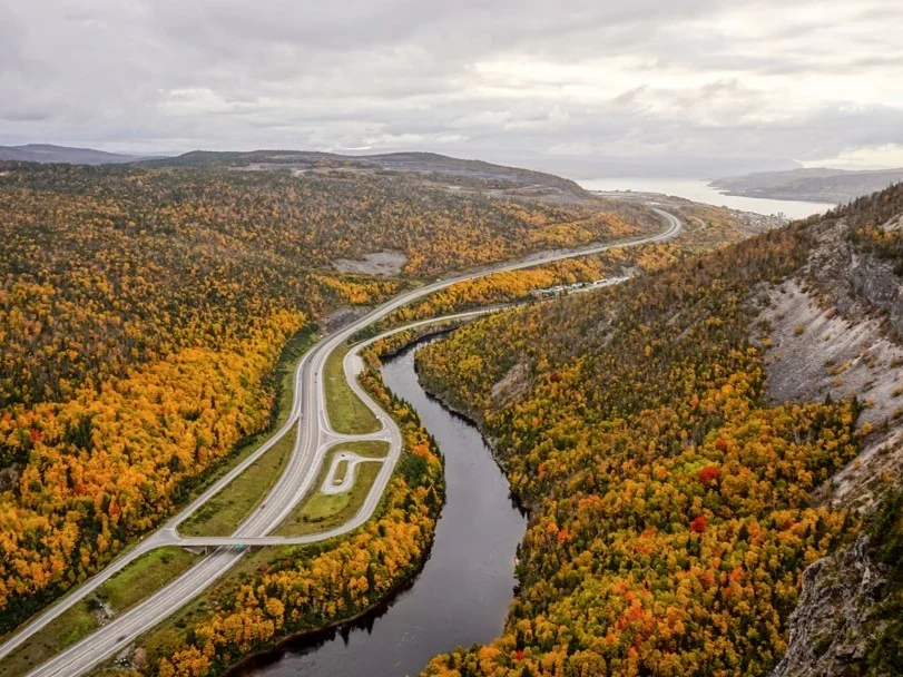 Kronkelende snelweg door een bos in herfstkleuren naast een rivier gezien vanuit de lucht met heuvels op de achtergrond