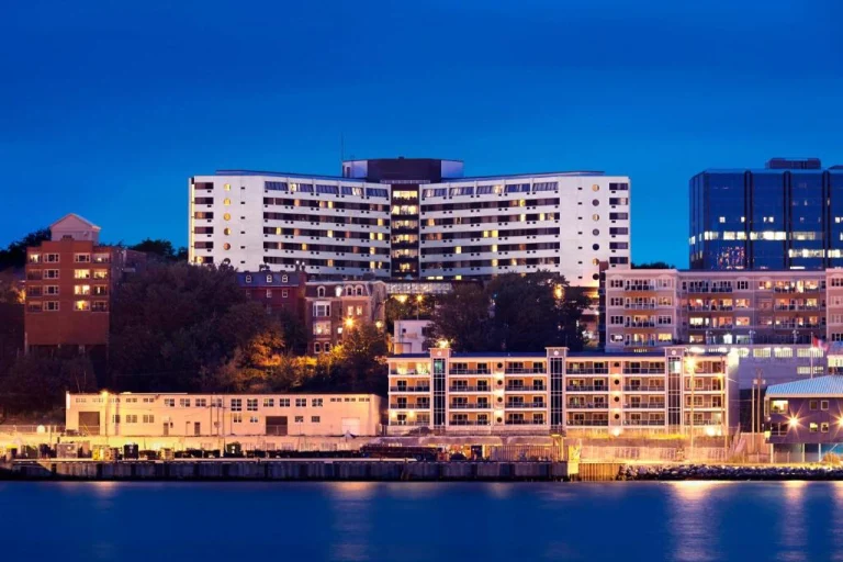 Verlichte gebouwen en een hoge toren aan de waterkant in de blauwe avondschemer met lichtjes die weerspiegelen in het water