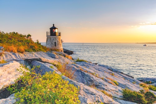 Stenen vuurtoren op een rotsachtige kaap met laag struikgewas, gefotografeerd bij zonsondergang in Newport in Rhode Island
