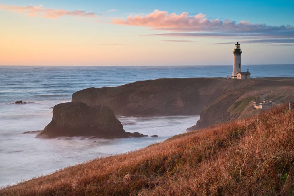 Witte vuurtoren Yaquina Head Lighthouse op een rotsachtige kaap met grasduinen op de voorgrond bij zonsondergang in Newport, Oregon