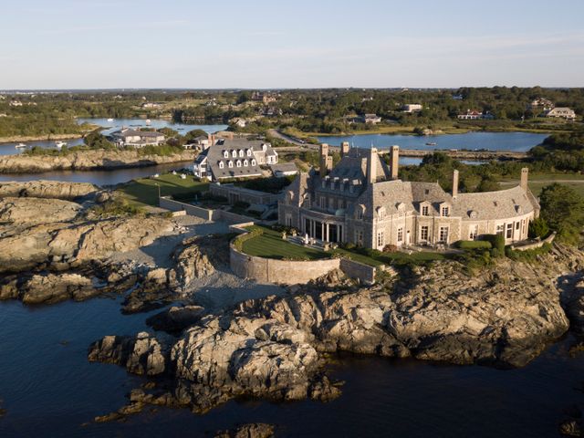 Luchtfoto van een groot stenen landhuis met torentjes op een rotsachtige landtong aan zee, omgeven door gazons en een muur bij Newport, Rhode Island
