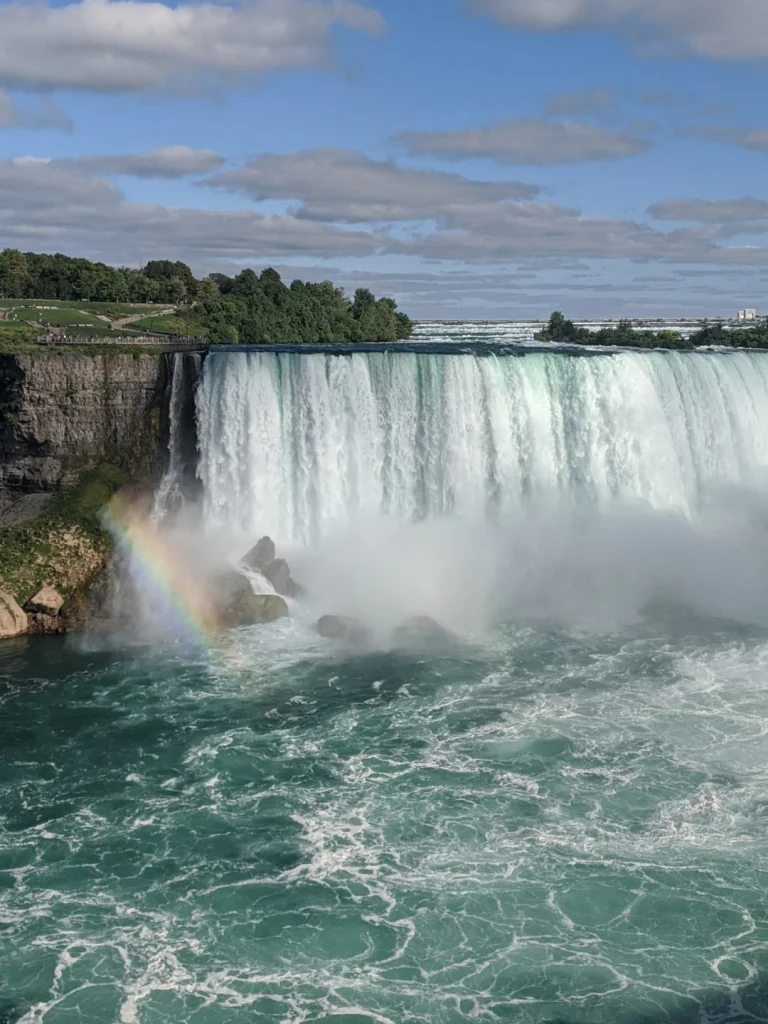 Krachtige waterval van Niagara Falls met rotsen en een regenboog in de opspattende nevel aan de voet, met turquoise water op de voorgrond