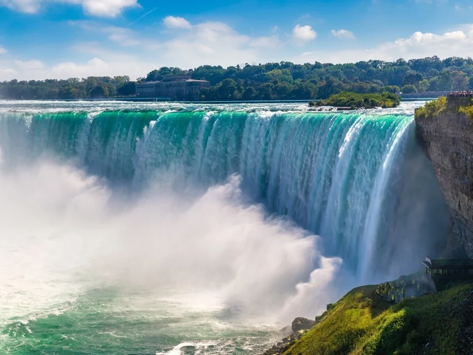 Brede hoefijzervormige waterval met turquoise water dat neerstort in een wolk van opspattend schuim, met groen op de kliffen