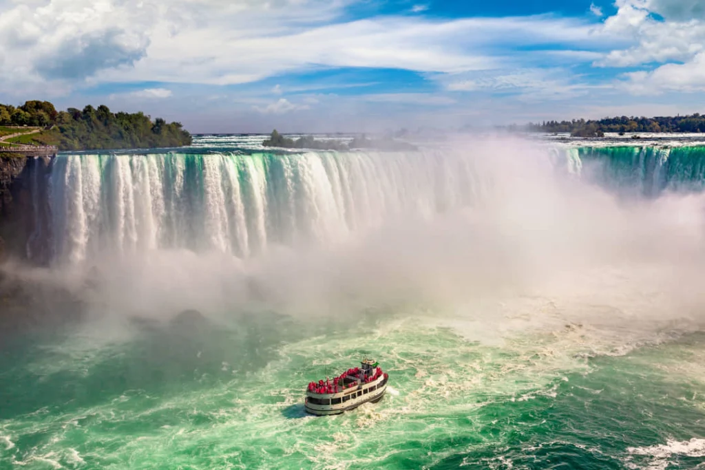 Een rood witte toeristenboot vaart door opspattend water vlak bij de kolkende Niagara watervallen